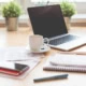Ein Arbeitsplatz mit Laptop, Handy, Notizbüchern, Stift und Kaffeetasse.