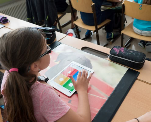 Ein Kind sitzt am Schultisch und hat ein Tablet vor sich liegen.