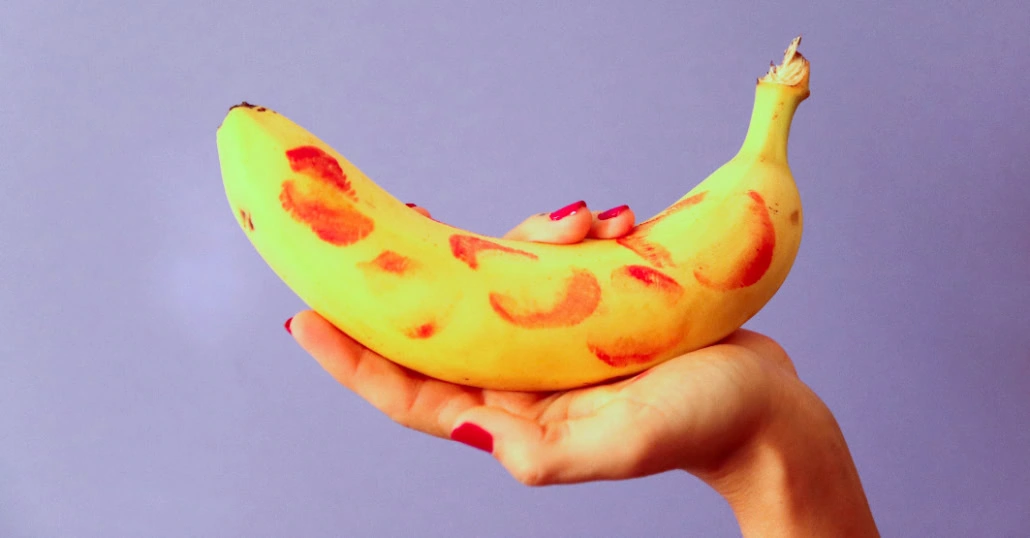 Hand mit rotem Nagellack hält eine Banane, auf der Abdrücke von Lippenstiftküssen zu sehen sind