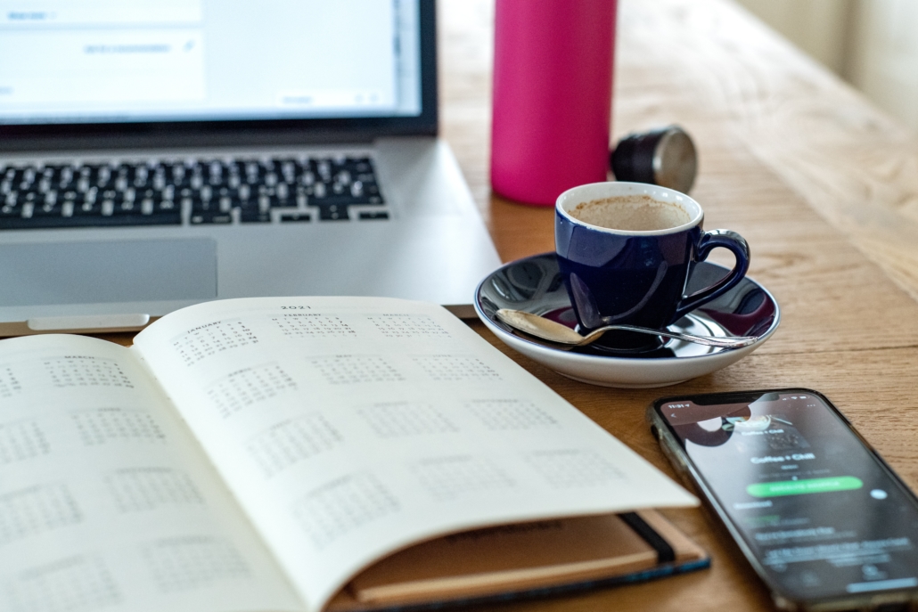 Ein Kalender, ein Smartphone, ein Laptop und eine Tasse Kaffee stehen auf einem Holztisch.