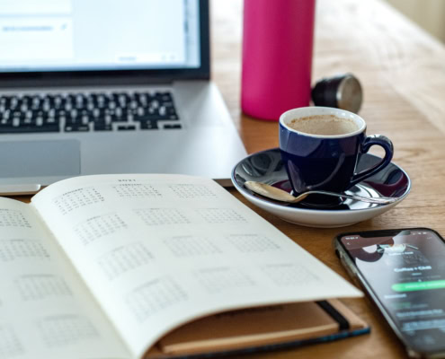 Ein Kalender, ein Smartphone, ein Laptop und eine Tasse Kaffee stehen auf einem Holztisch.
