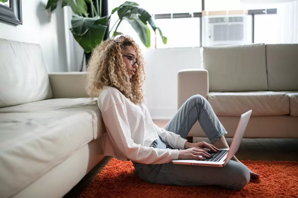 Eine Frau sitzt auf dem Boden und arbeitet an ihrem Notebook.