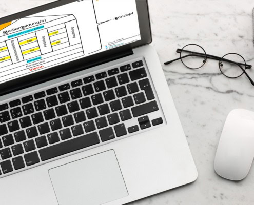 Ein Laptop, eine Brille und eine Computermaus liegen auf einem Tisch.