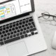 Ein Laptop, eine Brille und eine Computermaus liegen auf einem Tisch.