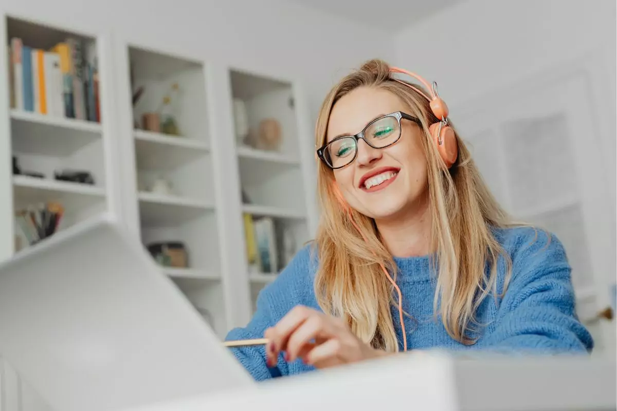 Frau mit blauem Pulli und Kopfhörern vor einem Laptop sitzend