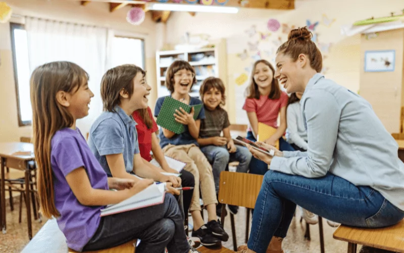 Lehrerin sitzt mit einigen Schüler*innen zusammen. Alle lachen.