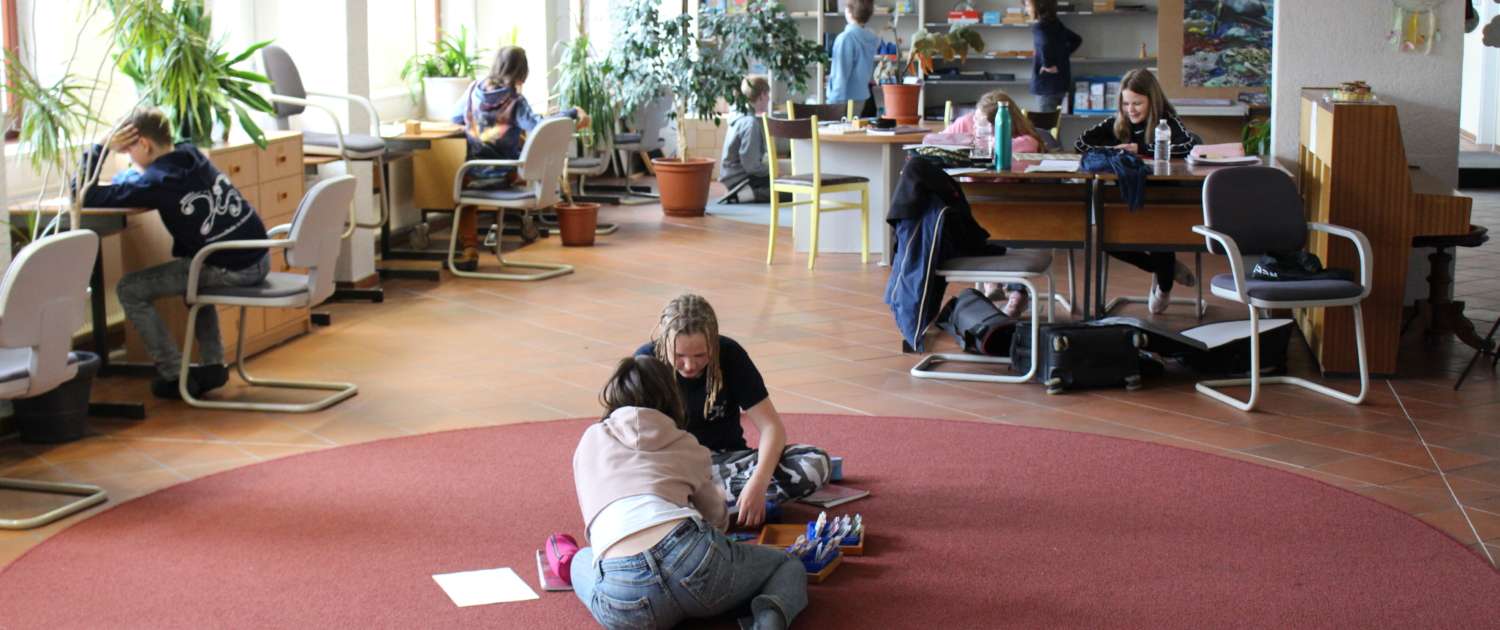 Schüler*innen sitzen auf dem Boden und lernen – andere Schüler*innen arbeiten an unterschiedlichen Lernorten